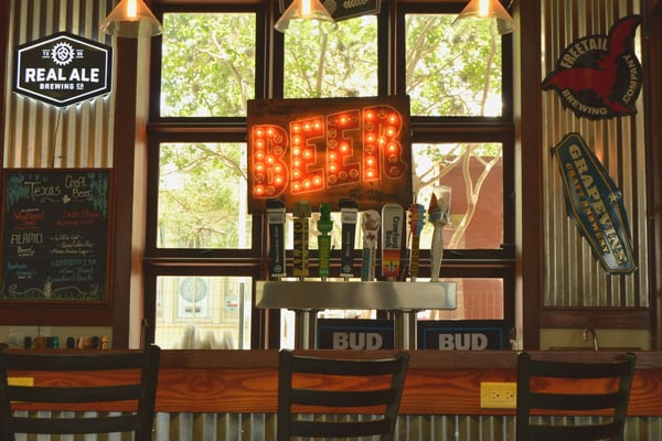 Warm taphouse bar interior with Real Ale Brewing signage and corrugated metal walls